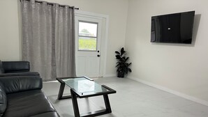 A living room with a black leather sofa, a glass-top coffee table, a potted plant, and a flat-screen TV mounted on the wall. - Spacious 4-bedroom , newly building in center of Hilo. (Hilo)