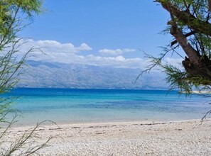A beach with clear water, pebbles, and distant mountains. - Mobile Home Nalani (Razanac)