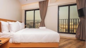 Ein Schlafzimmer mit Bett, Holzboden, großen Fenstern und einem Balkon.