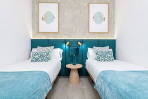 Une chambre avec deux lits, une petite table et deux tableaux encadrés au mur.