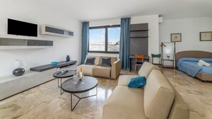 A modern living room with a sofa, a coffee table, a TV mounted on the wall, a bed, and a window with curtains. - Tenuta Marrocco House (Cursi)