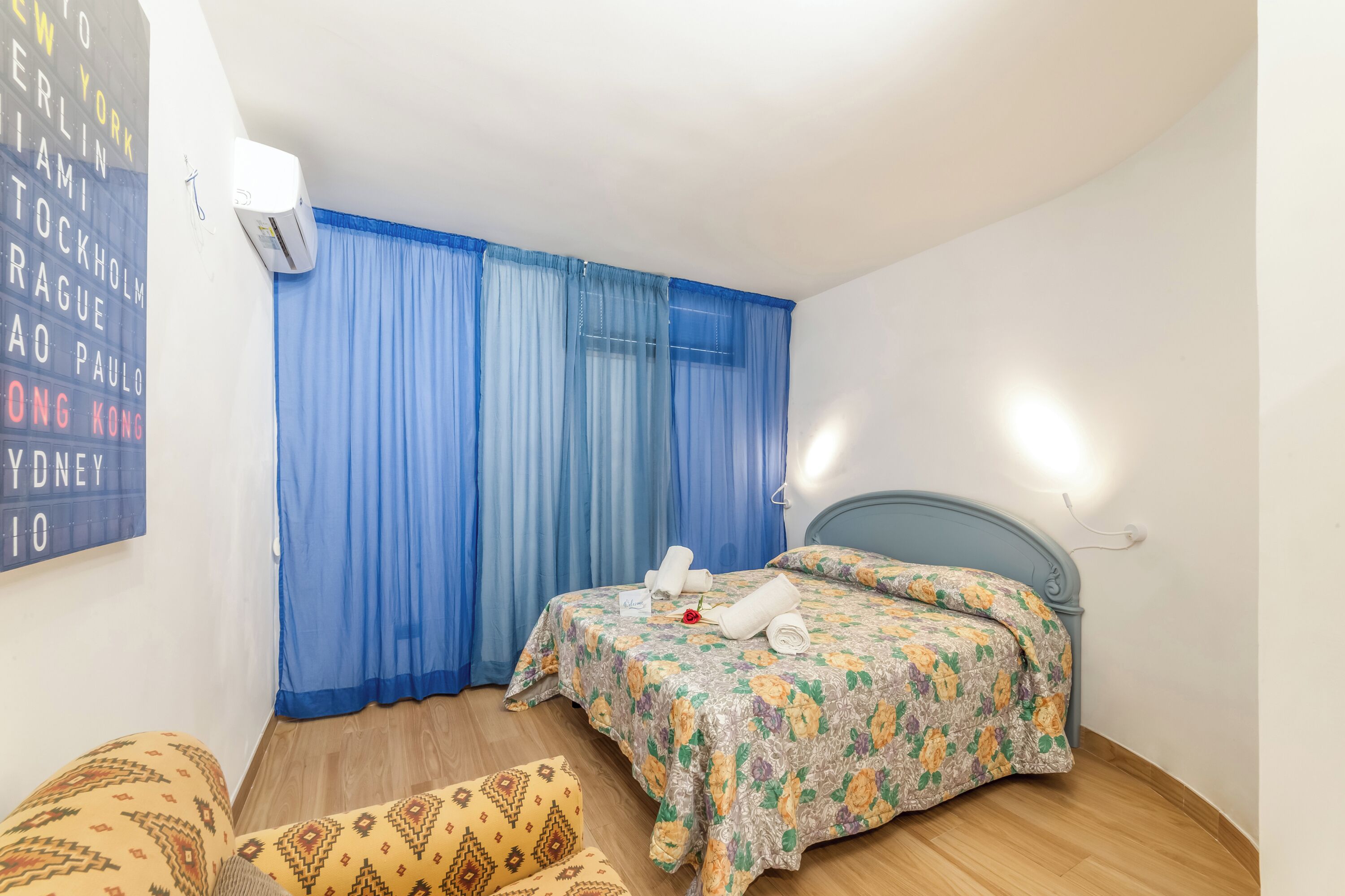 A bedroom with a bed, a chair, a wall-mounted air conditioner, and a curtain.
