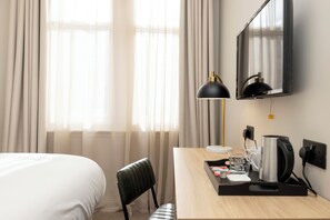 A hotel room with a bed, a desk with a lamp, a coffee maker, and a mirror. - Joivy Royal Mile (Edinburgh)