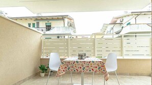 Een terras met een tafel, stoelen, een bloempot en uitzicht op gebouwen.