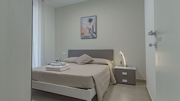Een slaapkamer met een bed, nachtkastje en een aan de muur hangend schilderij.