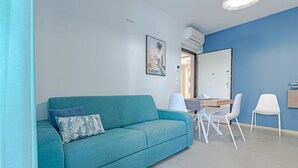 A modern living room with a teal sofa, a dining table with chairs, a large mirror, and a painting on the wall. - Homiday - Albatros 2, Two Bedroom Apartment on the Ground Floor (Alba Adriatica)