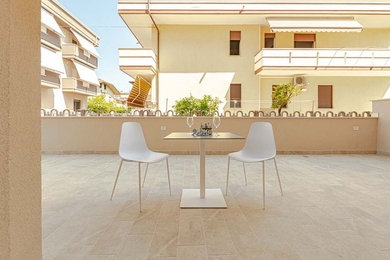 Une terrasse avec une table et deux chaises, un sol carrelé et, au fond, un immeuble doté de balcons.