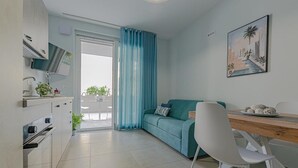 A modern kitchen with a dining area, a sofa, and a painting on the wall. - Homiday - Albatros 2, Two Bedroom Apartment on the Ground Floor (Alba Adriatica)