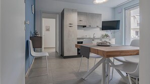 A modern kitchen with grey cabinets, a wooden dining table, and a flat-screen TV mounted above it. - Homiday - Albatros 2, Two Bedroom Apartment on the Ground Floor (Alba Adriatica)