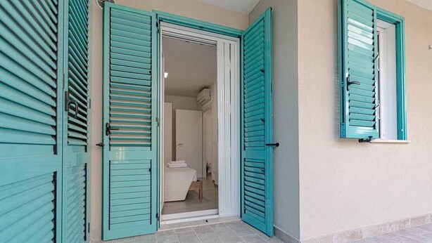 A room with teal shutters, a bed, and a bathroom visible through an open door. - Homiday - Albatros 3, Two Bedroom Apartment on the Ground Floor (Alba Adriatica)