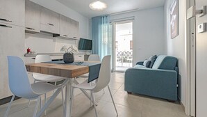 A modern kitchen with white cabinets, a dining table with chairs, a blue sofa, and a TV. - Homiday - Albatros 3, Two Bedroom Apartment on the Ground Floor (Alba Adriatica)