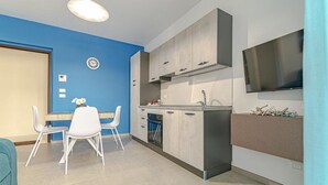 A modern kitchen with white cabinets, a dining area with white chairs, and a flat-screen TV mounted on the wall. - Homiday - Albatros 3, Two Bedroom Apartment on the Ground Floor (Alba Adriatica)