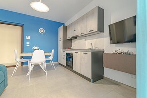 Eine moderne Küche mit weißen Schränken, ein Essbereich mit weißen Stühlen und ein an der Wand befestigter Flachbildfernseher.
