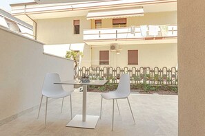 Une terrasse extérieure avec une table et deux chaises, une clôture blanche et un bâtiment avec des balcons en arrière-plan.