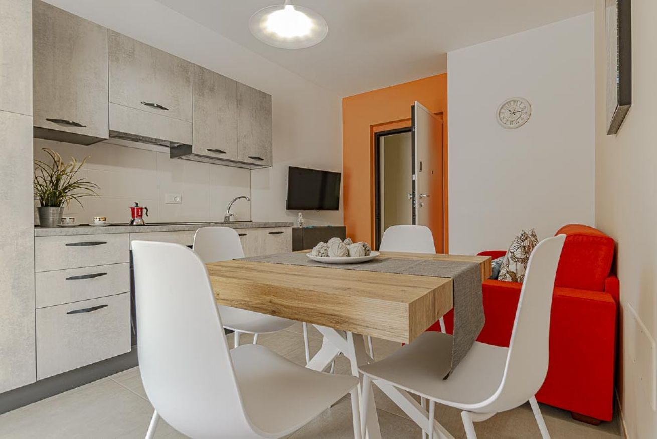 Une cuisine moderne avec des meubles gris, une table à manger en bois, des chaises blanches et un canapé rouge.