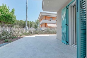A paved outdoor area with a building in the background, a fence, and a door with shutters. - Homiday - Albatros 5, Two Bedroom Apartment on the Ground Floor (Alba Adriatica)