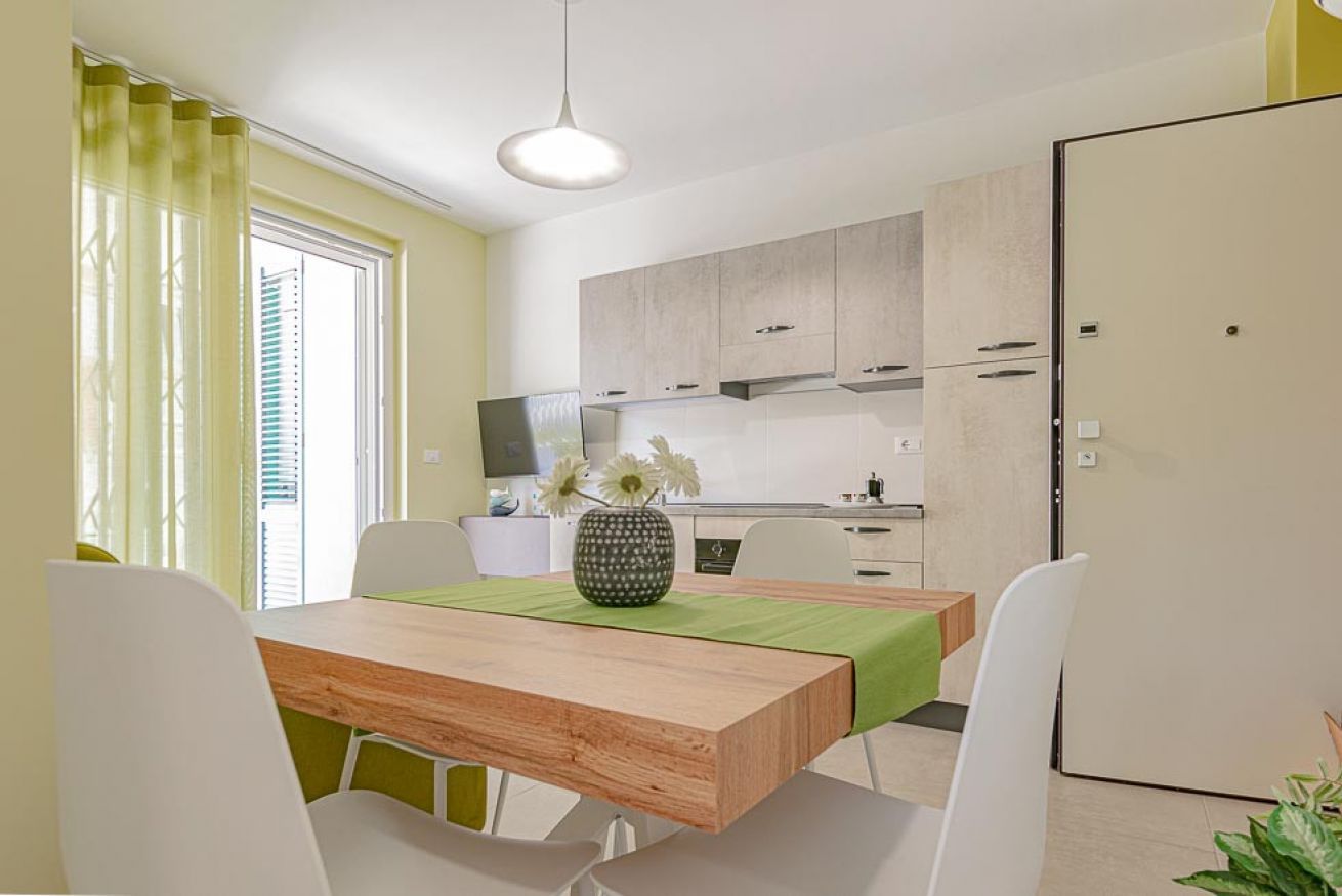 Une cuisine moderne avec des meubles blancs, une table en bois et une nappe verte.