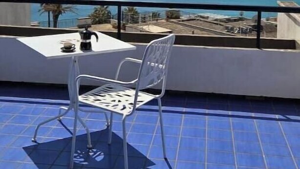 Een balkon met een tafel en stoel, met uitzicht op de kust.