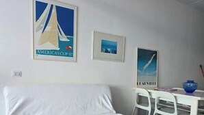 Een kamer met een witte bank, een eettafel met stoelen en twee ingelijste foto's aan de muur.