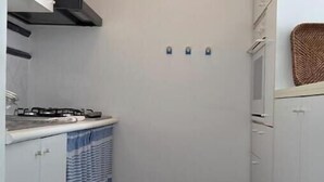 Een kleine keuken met een klok, een fornuis en een blauw gordijn met een patroon.