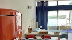 Une chambre avec un lit, une table et des chaises, un réfrigérateur rouge et une vue sur la mer.