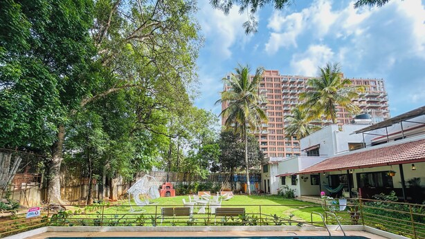 A swimming pool with a grassy area, a barbecue, and a building with balconies in the background. - Casa blu 4BHK Spacez Pool & Garden Villa (Bengaluru)