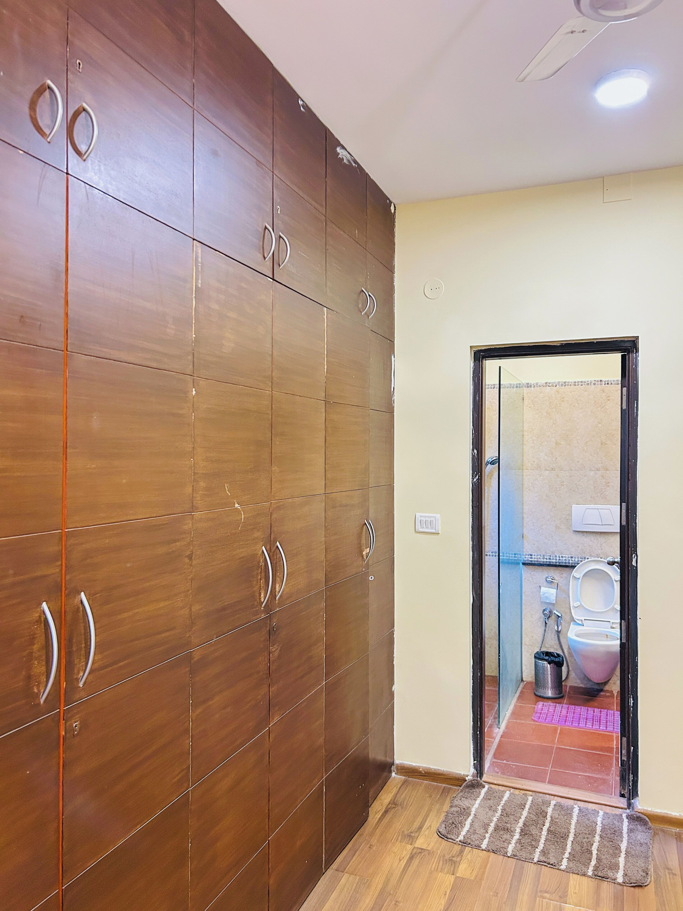 Een kamer met een grote inbouwkast, een deur naar een badkamer en een houten vloer.