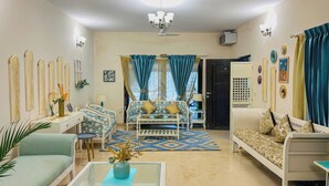 A living room with a sofa, chairs, a coffee table, a ceiling fan, and a TV. - Casa blu 4BHK Spacez Pool & Garden Villa (Bengaluru)