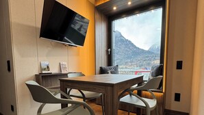 A modern dining area with a flat-screen TV mounted on the wall, a wooden table, and contemporary chairs. - Cube Alpine Stay (Buers)