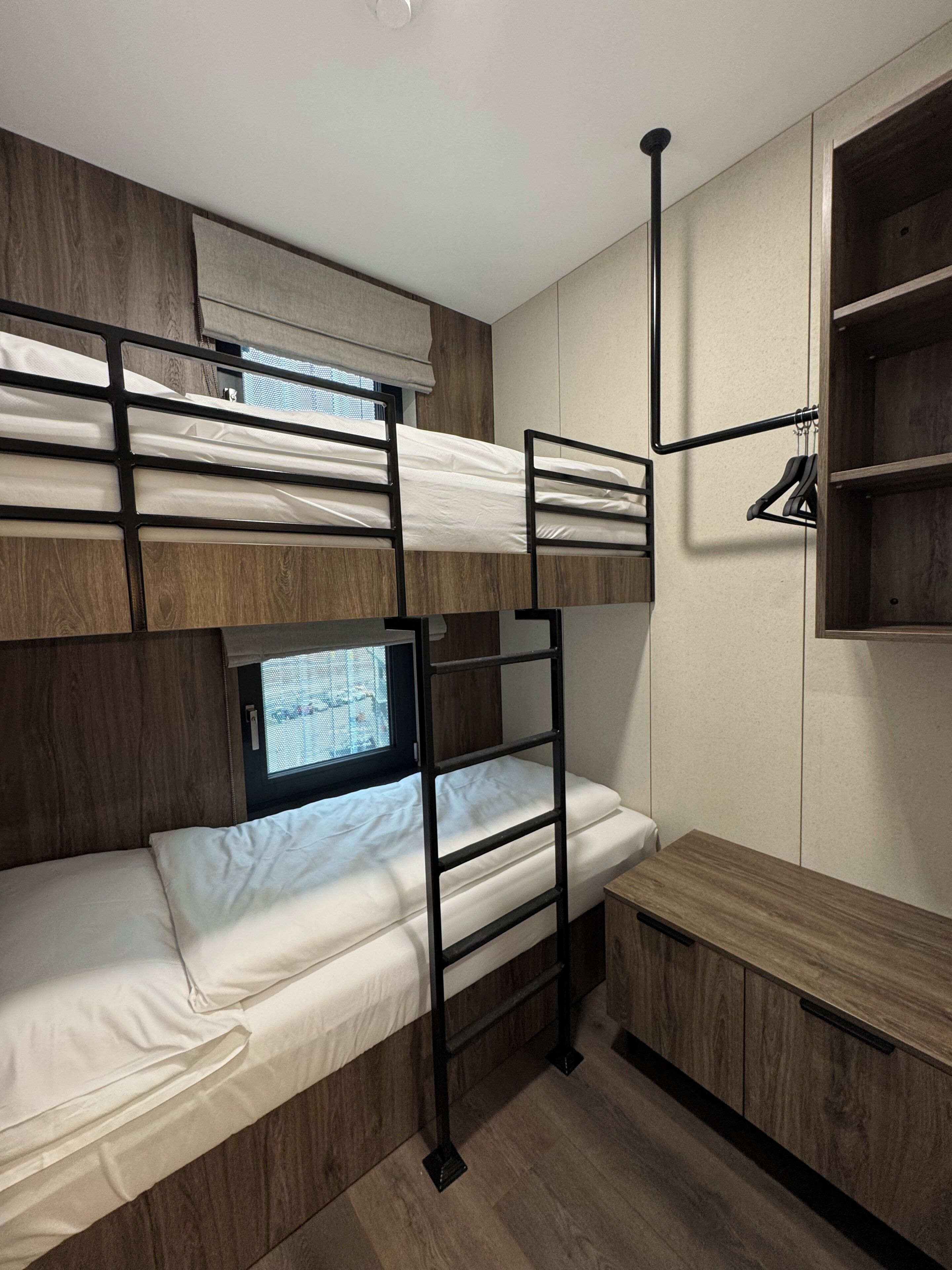 Une chambre avec un lit superposé, une fenêtre, un bureau et une armoire en bois.
