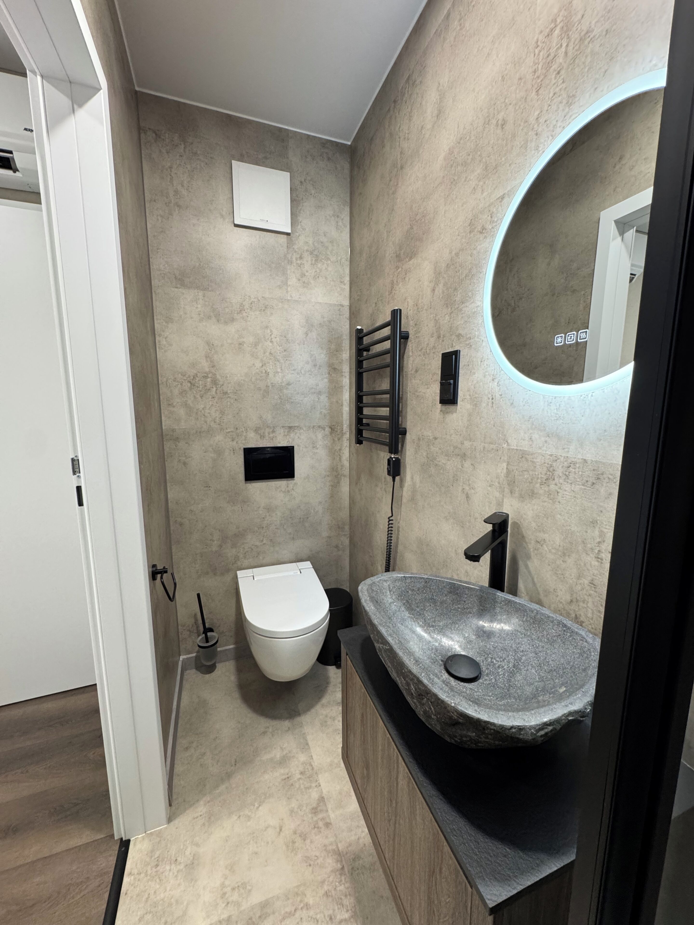 A modern bathroom with a stone sink, a toilet, a towel rack, and a mirror with a circular frame.