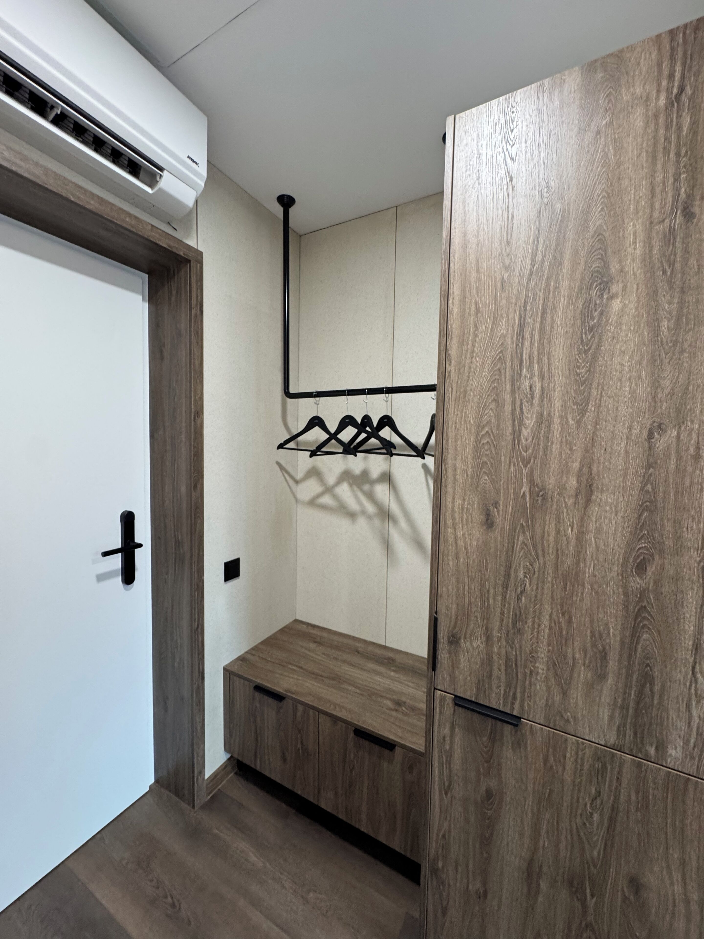 Un pasillo con un banco de madera, un perchero y una puerta blanca.