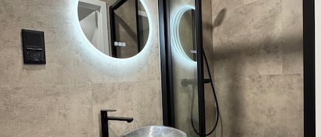 Un baño moderno con un lavabo de piedra, un espejo redondo y una ducha con cerramiento de vidrio.