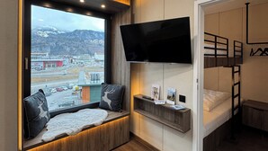 A modern room with a large window, a mounted TV, a bunk bed, and built-in shelves. - Cube Alpine Stay (Buers)