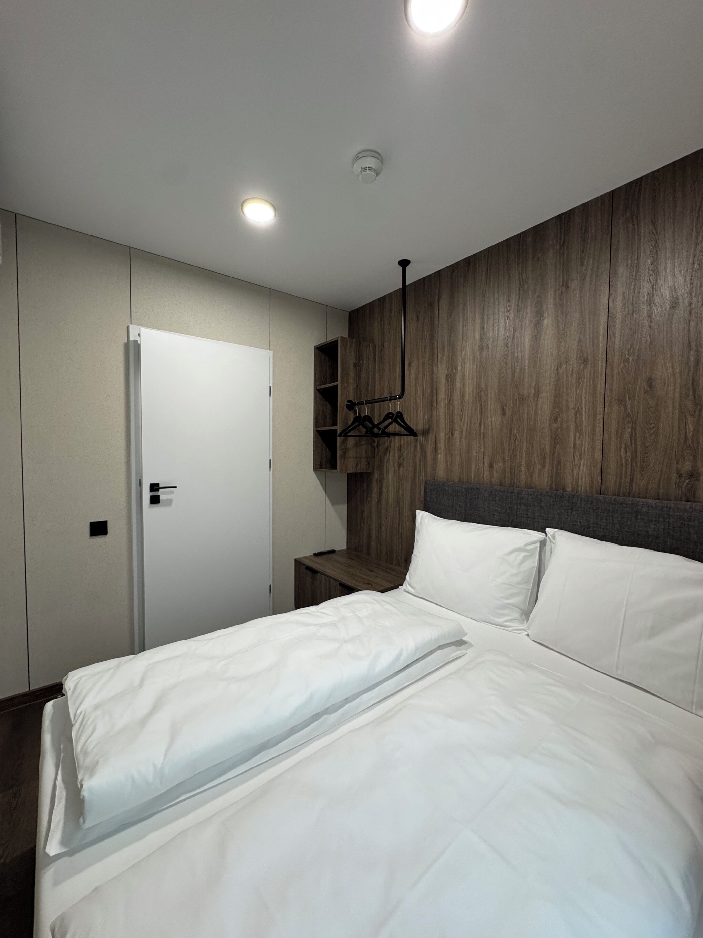 A modern bedroom with a bed, a wardrobe, a bedside table, and a wooden headboard.