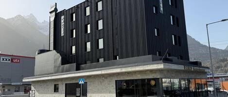 Een modern gebouw met een zwarte gevel, een inkom op straatniveau en een zichtbaar restaurantbord.