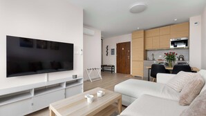 Un saló modern amb televisió plana, un sofà, una taula de centre i una zona de cuina amb armaris de fusta i microones.