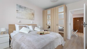 Un dormitori amb un llit, taules de nit, un armari i una porta que dona a una altra habitació.