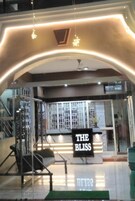 A hotel entrance with a sign reading 'THE BLISS,' a reception desk, and a staircase leading to the upper floors.