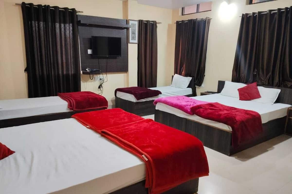 Ein Hotelzimmer mit drei Betten, jedes mit einer roten Decke, einem wandmontierten Flachbildfernseher und dunklen Vorhängen.
