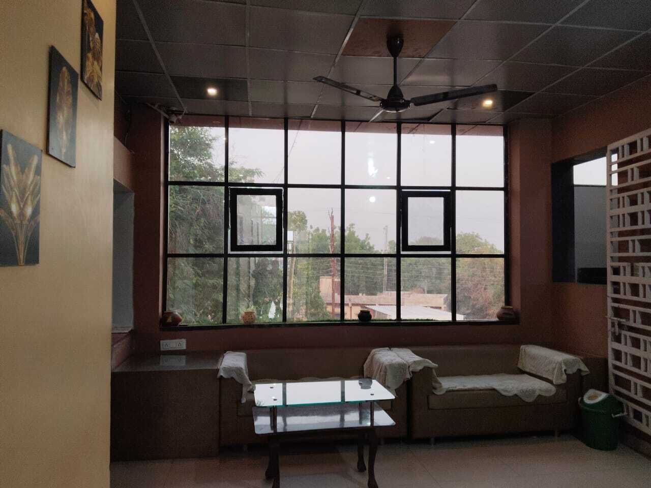 A room with a large window, a ceiling fan, a bench, and a small table.