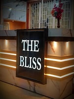 A reception desk with a sign that reads 'THE BLISS' and a vase with flowers on top.