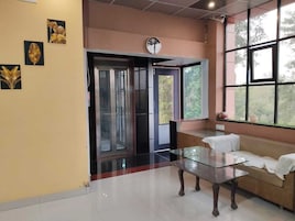 A room with a glass table, a sofa, a clock on the wall, and a window with a view of trees.