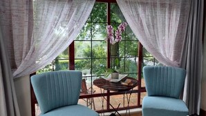 Una habitación con dos sillas azules, una mesita redonda y un ventanal con cortinas.