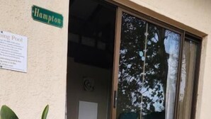 Entrada de un edificio con un letrero que dice 'Hampton', una puerta corrediza de vidrio, un escalón pequeño que lleva a la puerta y una planta en maceta.