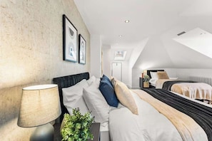 Una habitación de hotel moderna con techo estilo loft, una cama con muchas almohadas, una mesita de noche con lámpara y cuadros en la pared.