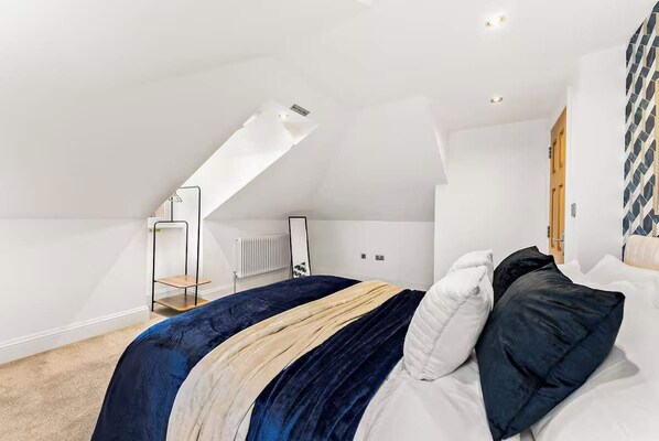 Un dormitorio con techo inclinado, una cama con manta a rayas, un radiador y una puerta.
