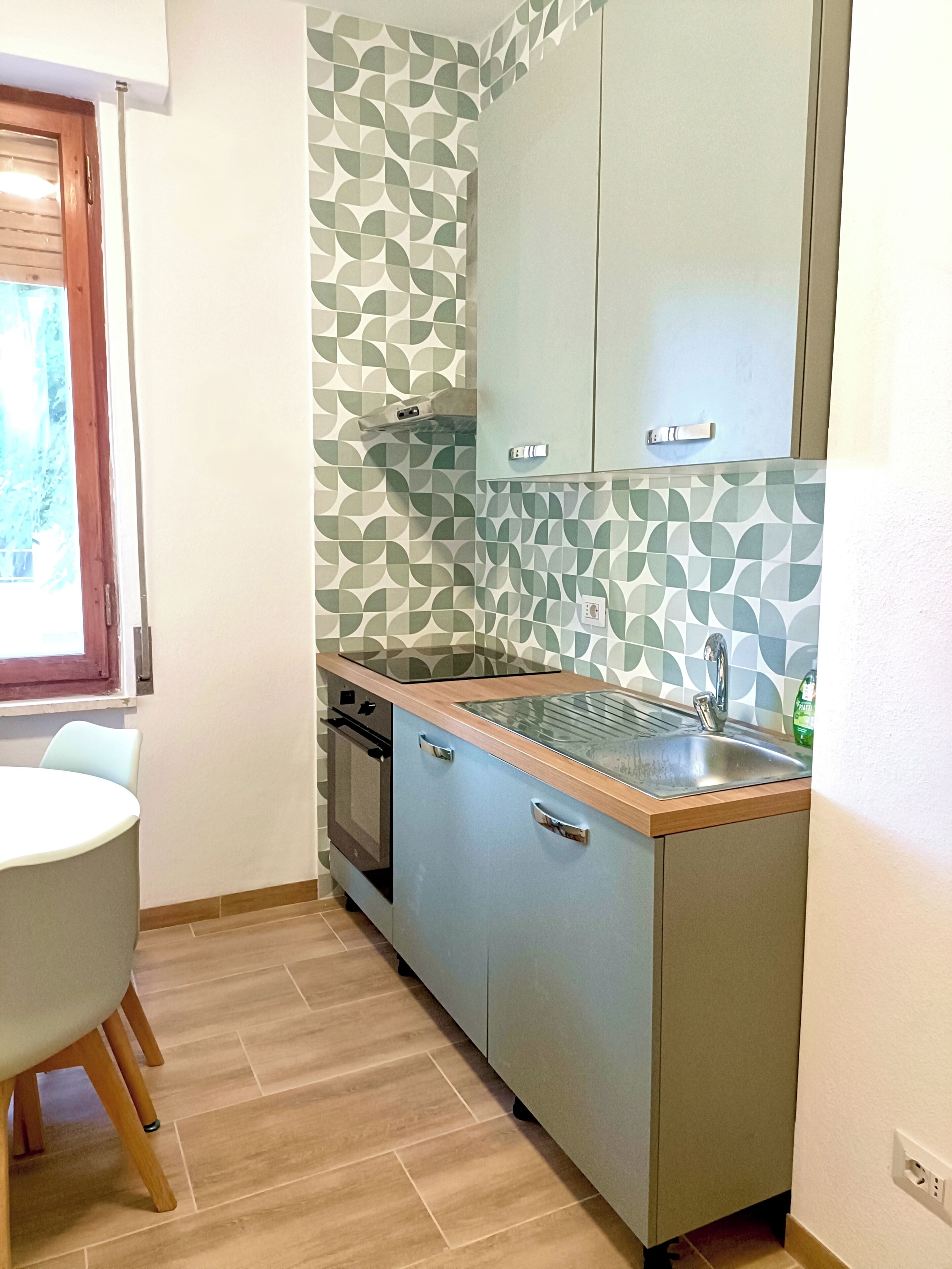 Una cocina compacta con horno integrado, un lavamanos y una ventana con persianas.