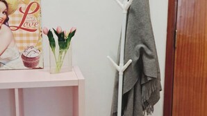 Une pièce avec une étagère rose, un porte-manteau blanc sur lequel est accroché un vêtement gris, une affiche représentant un cupcake et portant l’inscription « Aime, ris, aime », et une porte en bois.