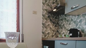 Une cuisine avec un mur de crédence à motifs, une machine à café et une fenêtre avec un rideau.